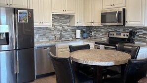 Una cocina moderna con armarios blancos, electrodomésticos de acero inoxidable, salpicadero de azulejos y una mesa de comedor redonda con sillas.