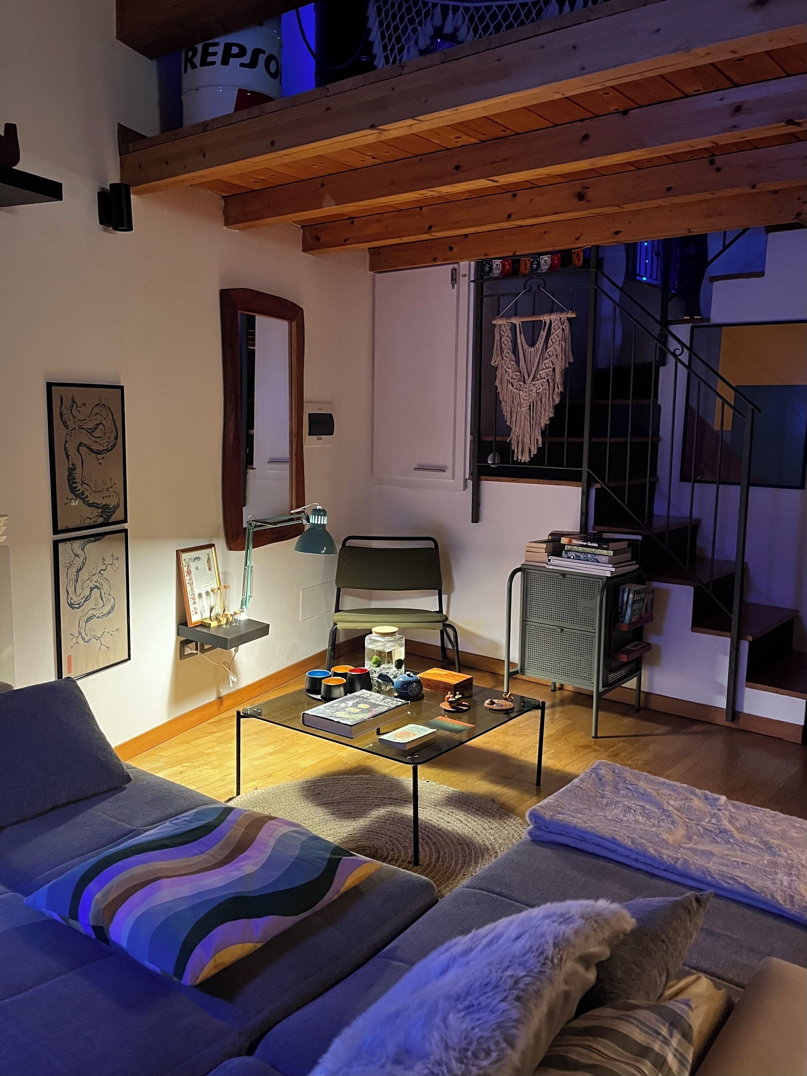 Ein gemütliches Wohnzimmer mit einer Couch, einem Couchtisch mit Büchern und Dekoration, einem Sessel und einer Treppe, die in eine obere Ebene führt.