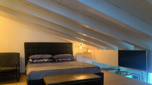 Ein Schlafzimmer mit Bett, Nachttisch, Sessel und Fernseher.