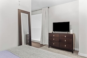 A bedroom with a bed, a dresser, a television, and a window with curtains.