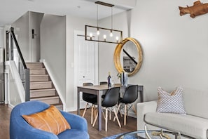 A modern living room with a blue armchair, a white sofa, and a dining area with a wooden table and chairs.