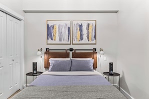 A bedroom with a bed, two bedside tables, a headboard, and two abstract paintings on the wall.