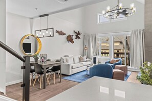 A modern living room with a dining area, a staircase, and a view of the outside.