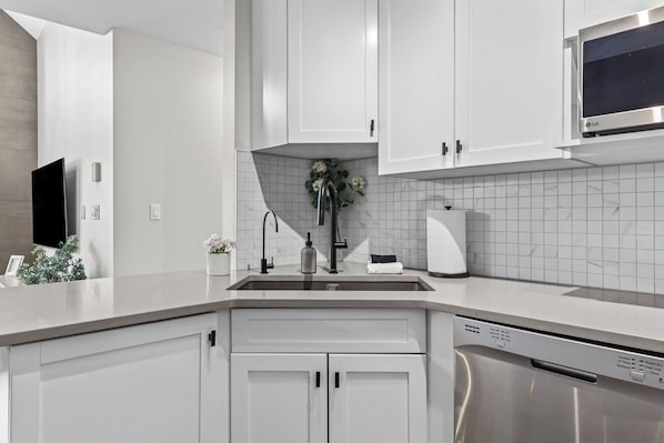 A modern kitchen with white cabinetry, a stainless steel microwave, and a dishwasher.