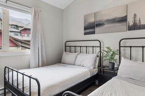 A bedroom with two single beds, a window with a view of buildings, and a plant on a bedside table.