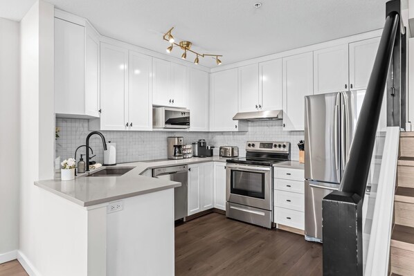A modern kitchen with white cabinetry, stainless steel appliances, and a wooden floor.