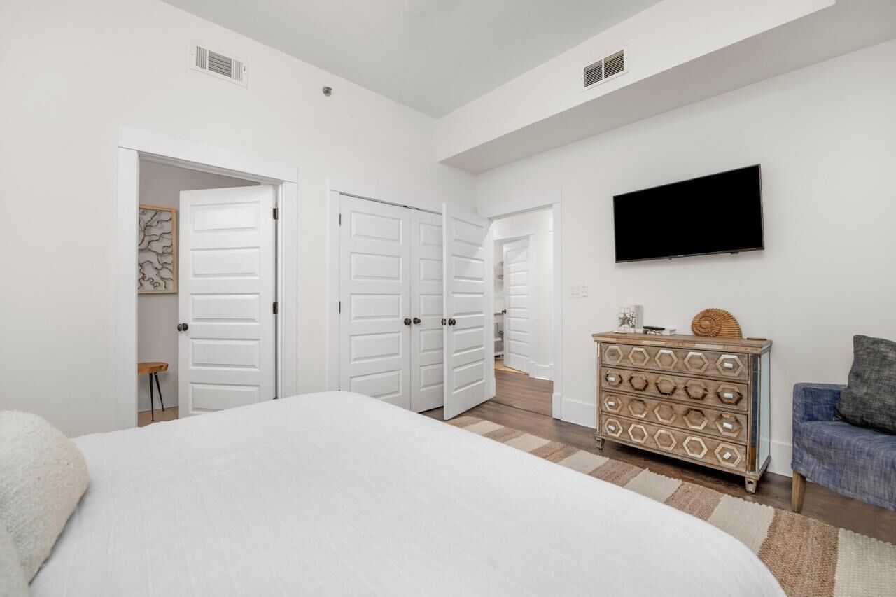 A bedroom with a large bed, white walls, a flat-screen TV, a dresser, and a sofa.