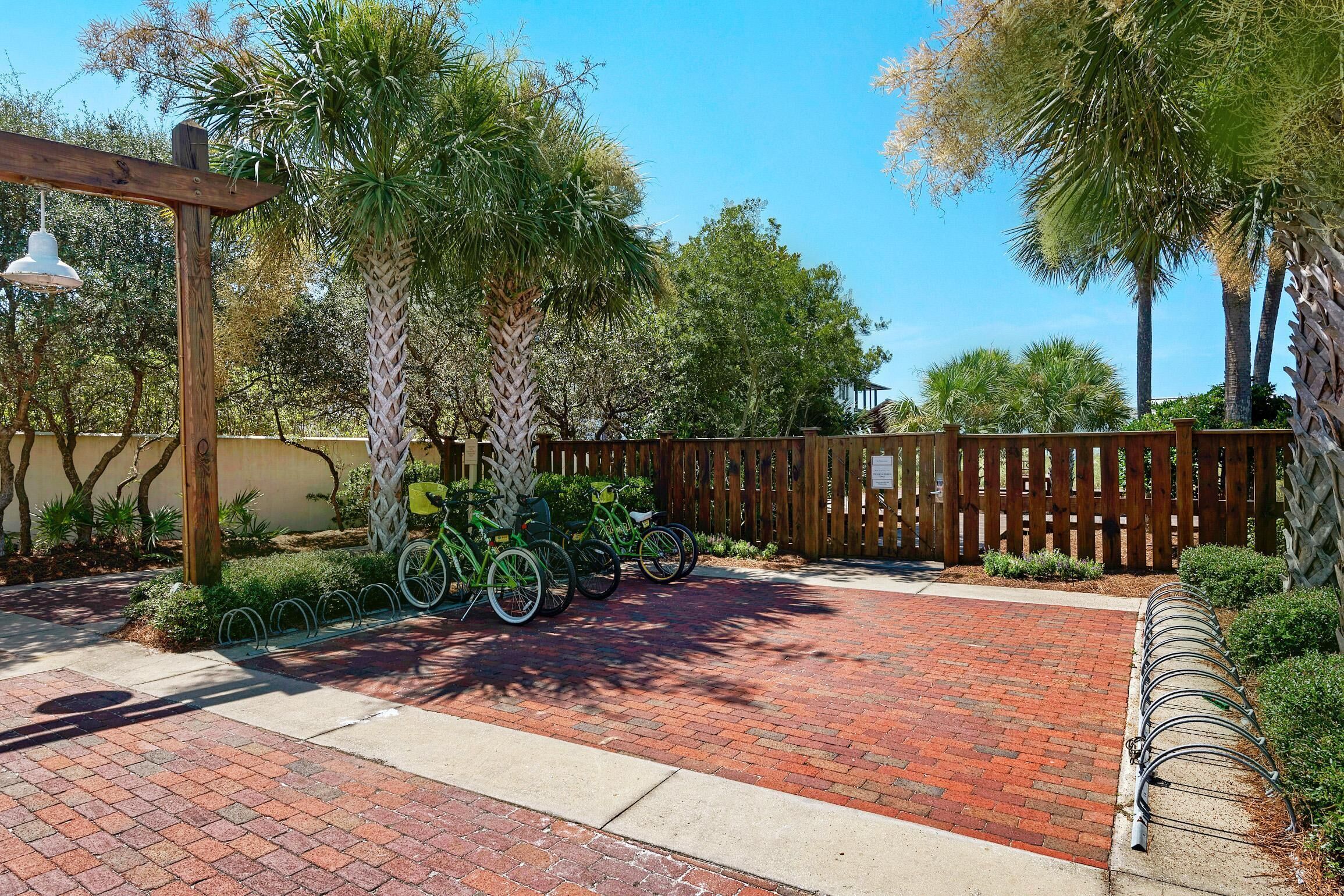 A paved driveway with bicycles parked on the side, a wooden pergola, and a wooden fence.