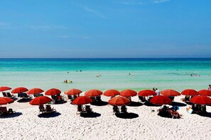 En strand med röda parasoller och vit sand.