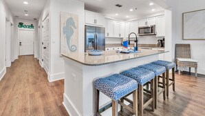 A modern kitchen with white cabinets, a stainless steel refrigerator, a microwave, and a large island with bar stools. - Redfish Village M2321- Changes in Latitude (Santa Rosa Beach)