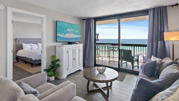 A room with a bed, a sofa, a dining table, a painting, and a balcony with a view of the sea. - Sundestin 1818 (Destin)