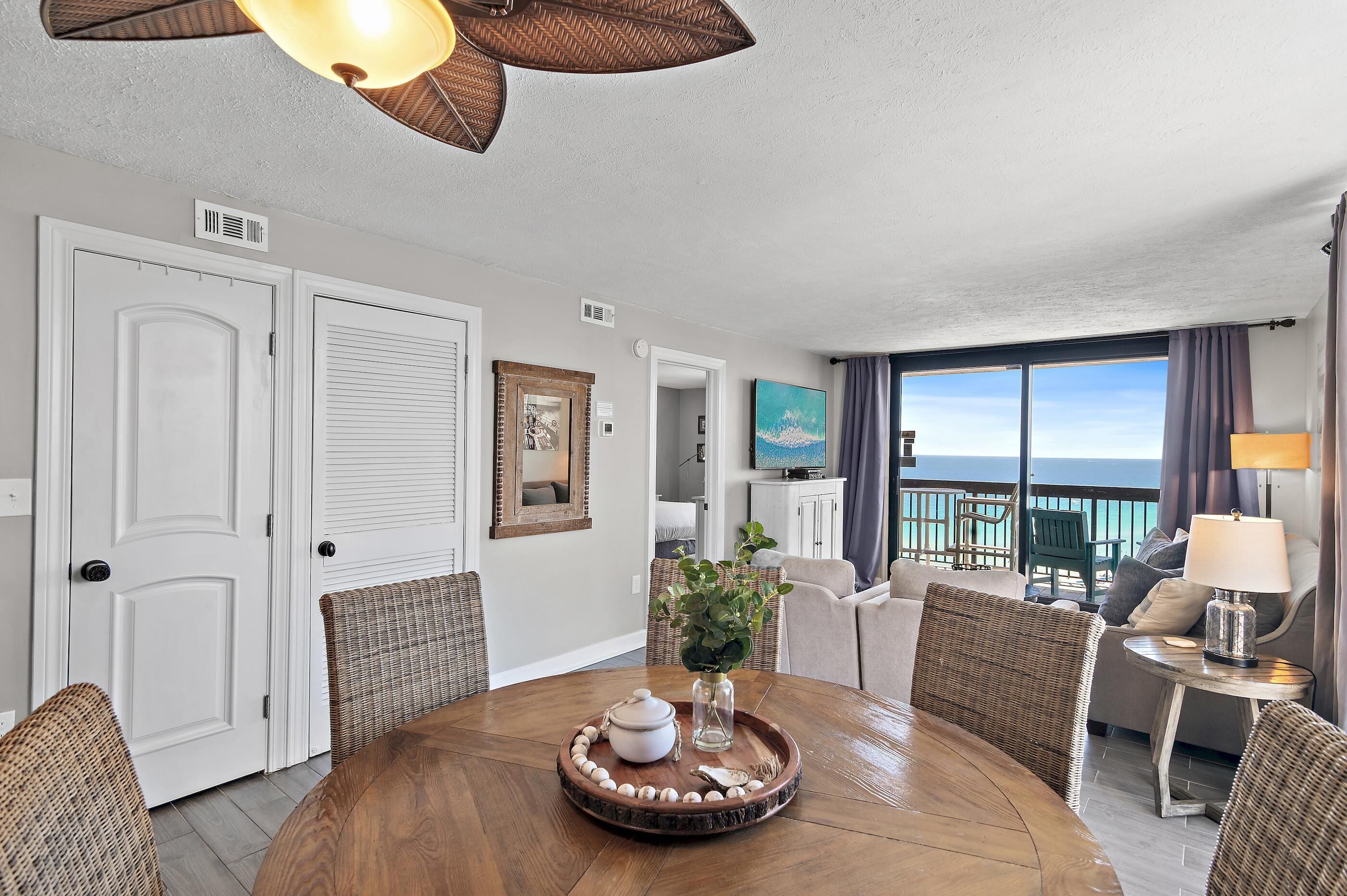A dining area with a round table, wicker chairs, and a view of the ocean through large windows.