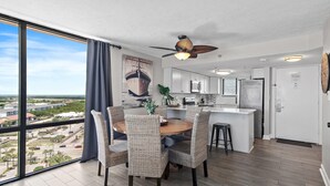 A modern kitchen with white cabinets, a central island, and a dining area with wicker chairs. - Sundestin 1818 (Destin)
