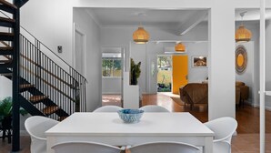 A modern interior with a staircase, a dining area with a white table and chairs, and a bright orange accent wall. - The Lazy Mimosa Beach Escape Fishing, Bikes & Cozy Firepit (Budgewoi)