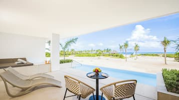 A modern lounge with a curved bench, two wicker chairs, a round table with fruit, and a poolside view.