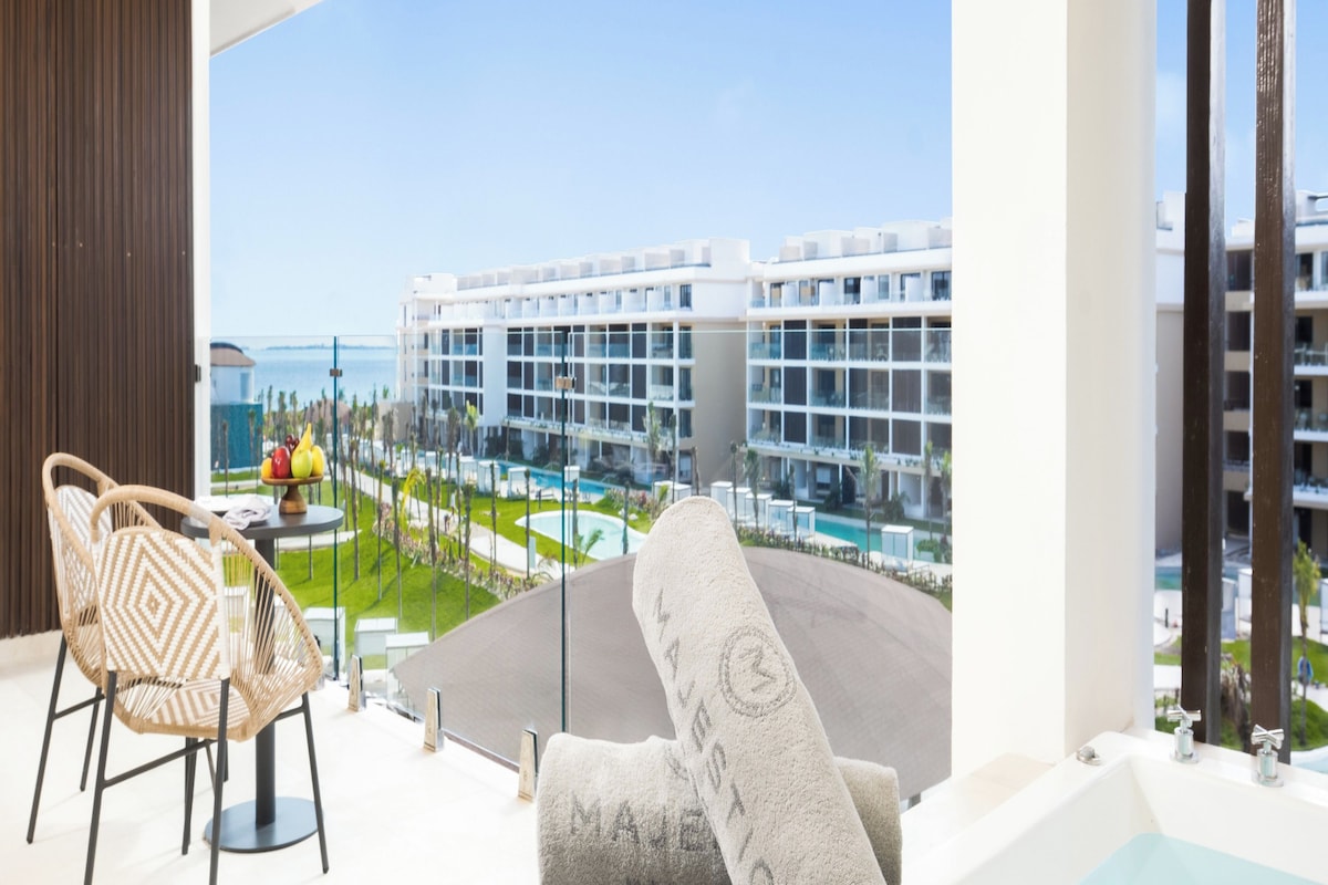 A modern hotel room with a balcony, a pool, and a view of a resort complex.