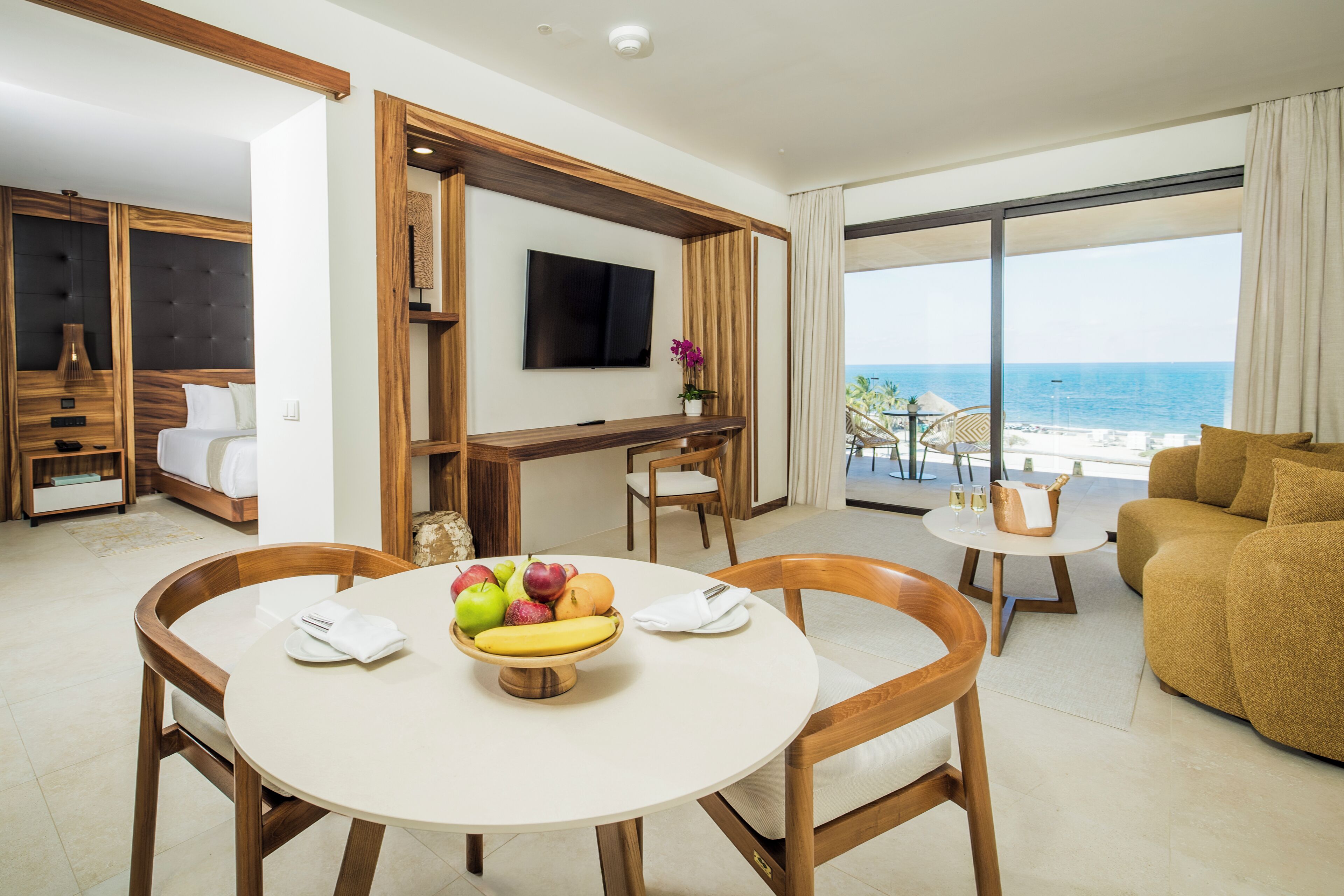 A hotel room with a dining area, a TV, and a view of the ocean.