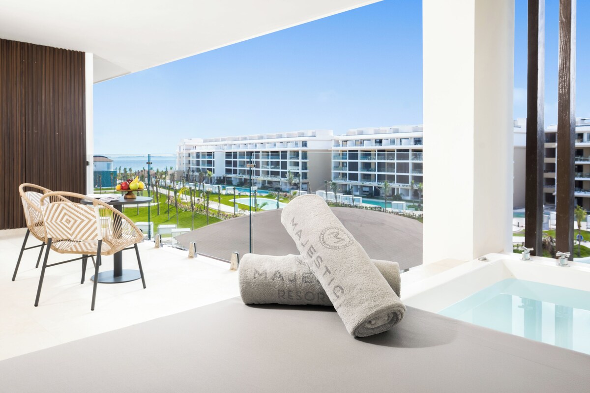 Une chambre d’hôtel moderne avec balcon, piscine et vue sur un complexe hôtelier.