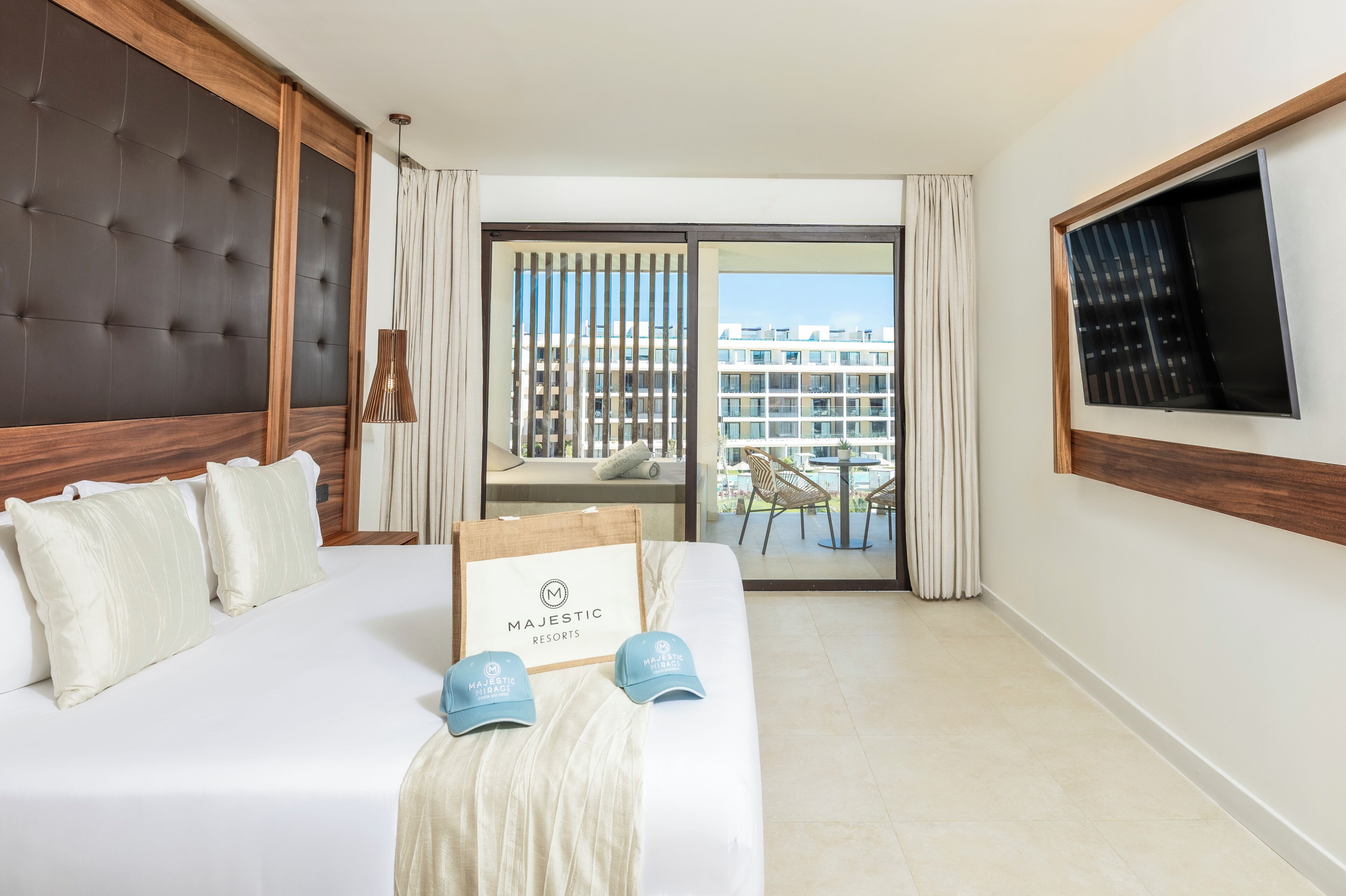 A hotel room with a large bed, a TV mounted on the wall, and a view of the city through the window.