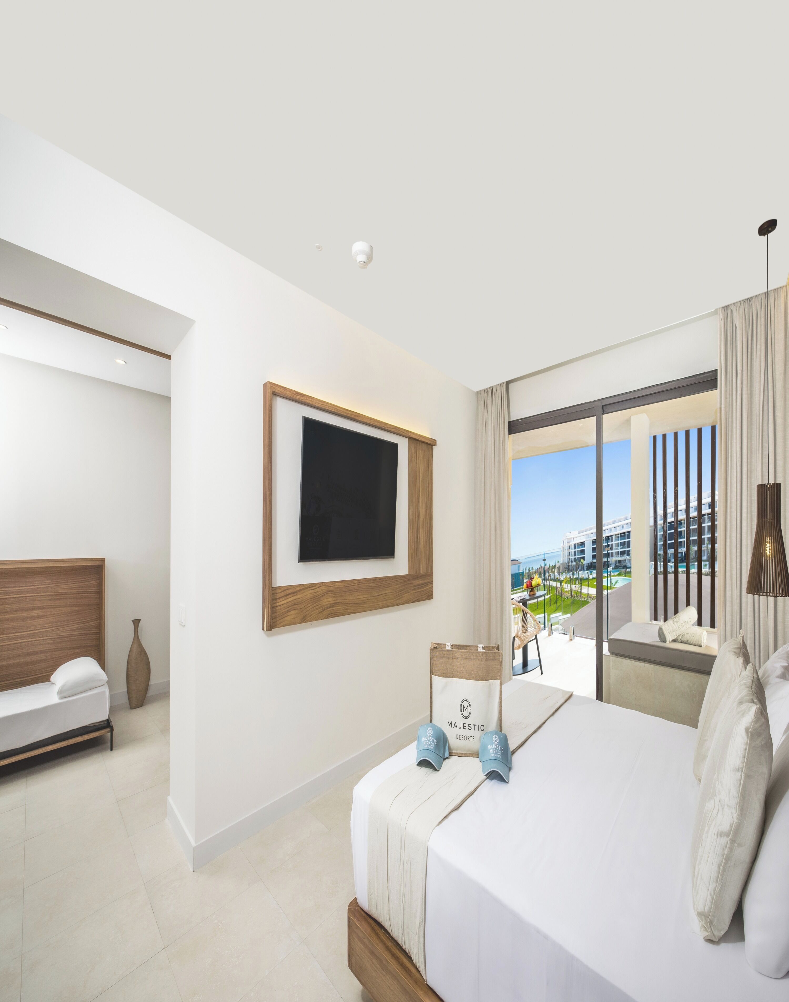 Una habitación de hotel moderna con una cama grande, un televisor de pantalla plana montado en la pared, vistas a la ciudad y un amplio ventanal con cortinas.