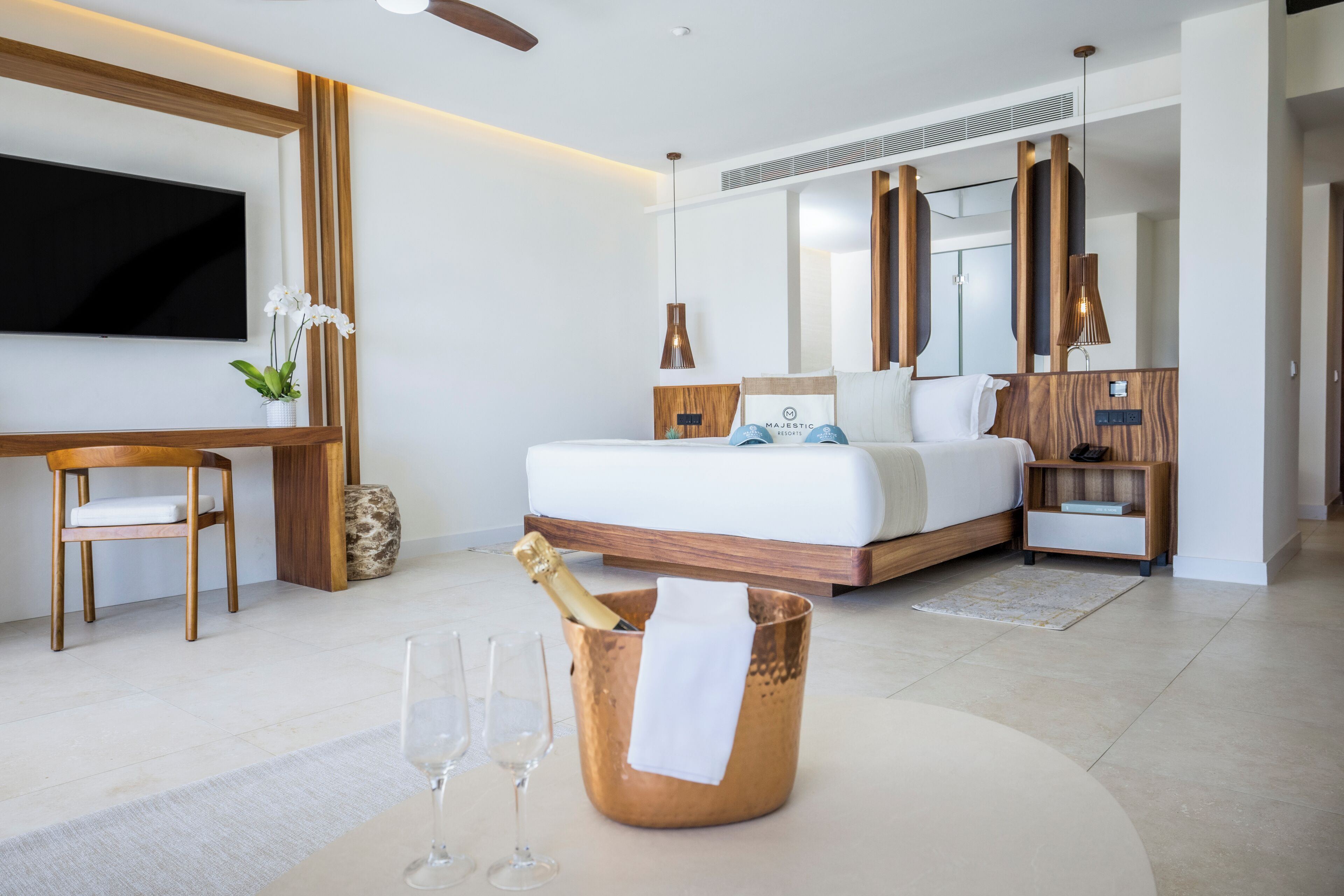 A modern hotel room with a large bed, a television, a wooden desk, and a minibar.