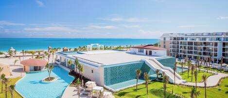 A resort with a swimming pool, palm trees, and a view of the ocean.
