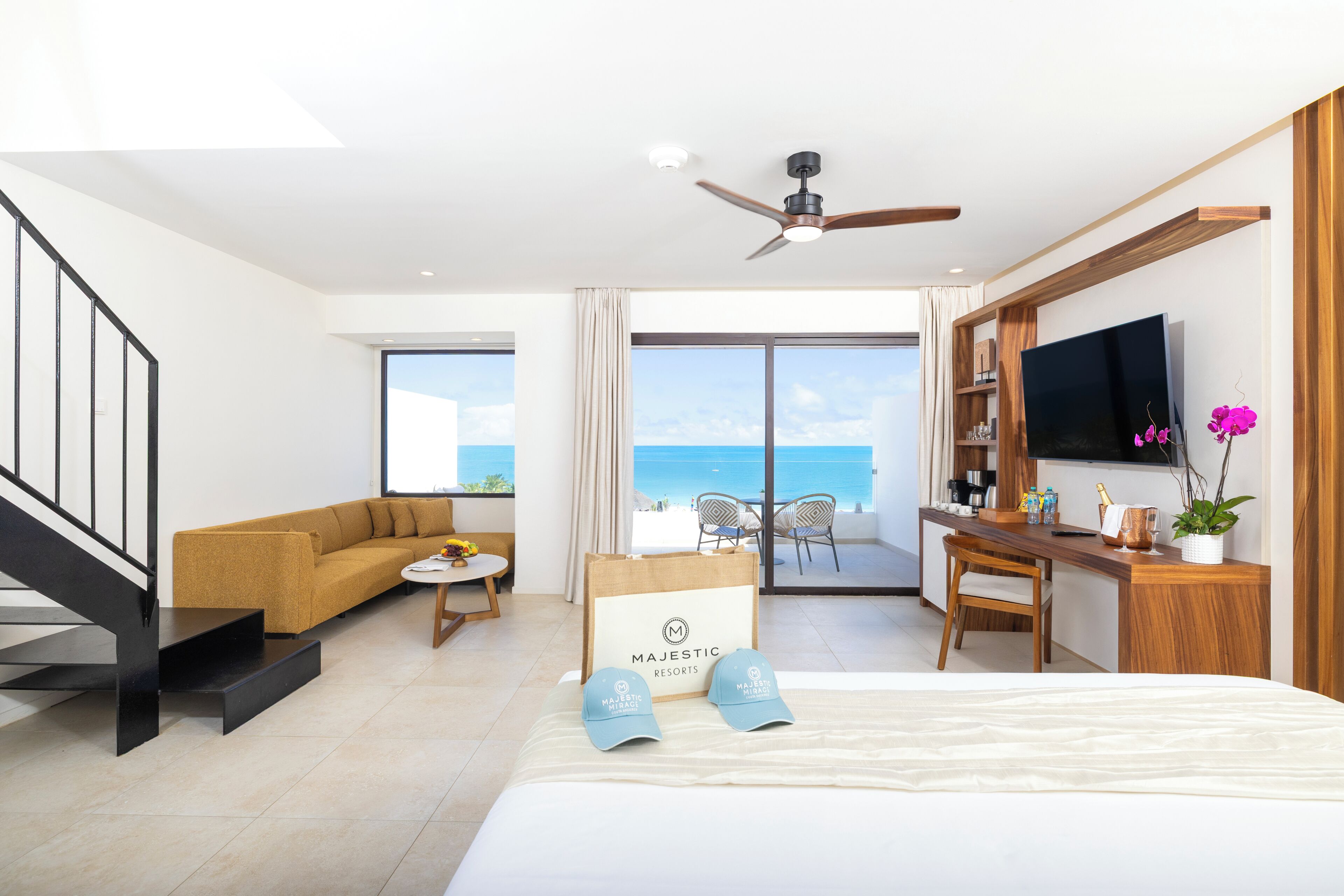 A hotel room with a bed, a desk, a sofa, a TV, and a balcony with a view of the sea.