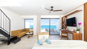 Habitación de hotel con cama, escritorio, sofá, televisor y balcón con vista al mar.