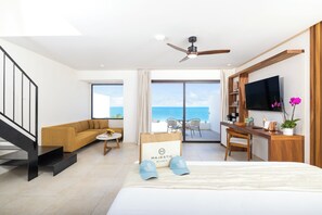 Habitación de hotel con cama, escritorio, sofá, televisor y balcón con vista al mar.