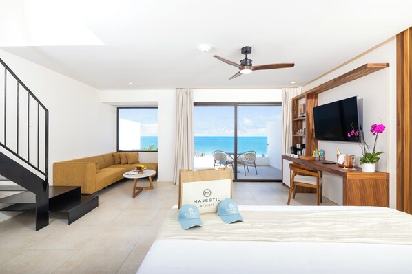 Habitación de hotel con cama, escritorio, sofá, televisor y balcón con vista al mar.