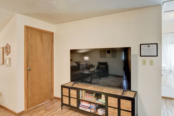 Una habitación con una puerta de madera, un televisor sobre un soporte de metal negro y un certificado enmarcado en la pared.