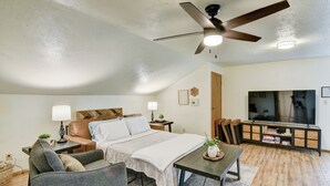 A bedroom with a bed, a desk, a chair, a TV, and a ceiling fan.