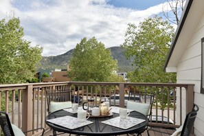 A balcony with a round table set for tea, surrounded by chairs, overlooking a mountainous landscape.