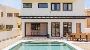 Una casa moderna de dos pisos con piscina, mobiliario exterior y un patio cubierto.