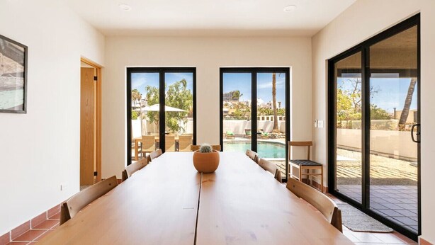 Una habitación amplia con una larga mesa de madera, ventanas grandes y vistas a una piscina y zona exterior.