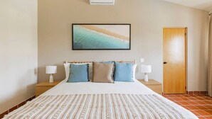 Una habitación de hotel con una cama grande, dos mesitas de noche con lámparas, una puerta de madera y un cuadro enmarcado en la pared.