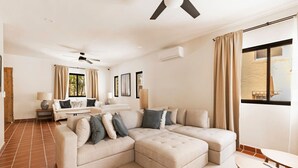 Una sala moderna con un sofá seccional, una mesita redonda y un ventilador de techo.