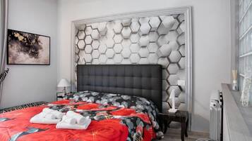 A modern hotel room with a geometric-patterned headboard, a neatly made bed with a red and black floral bedspread, and a side table with a lamp.