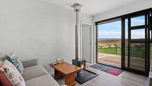Un salon moderne comprenant un canapé, une table en bois, une cheminée et une grande porte-fenêtre coulissante donnant sur un paysage extérieur magnifique.