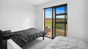 Une chambre avec deux lits, une grande porte-fenêtre coulissante donnant sur une terrasse et une vue sur un paysage verdoyant.