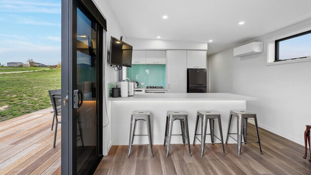 Une cuisine moderne dotée d’un îlot central, de tabourets de bar et d’une grande fenêtre donnant sur un espace verdoyant.