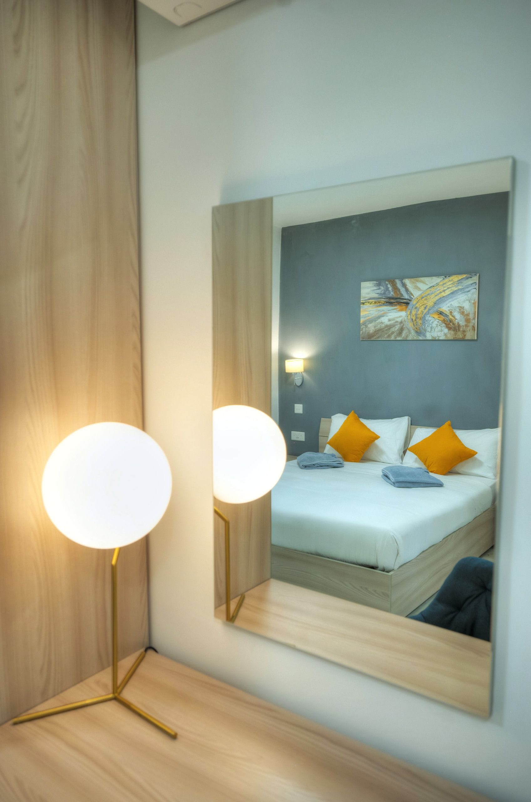 Una habitación de hotel con una cama, dos lámparas de noche, una mesita de noche, un espejo en la pared y un cuadro.