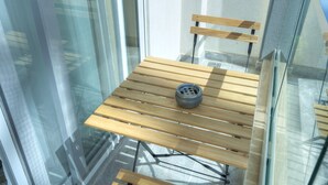 A wooden bench with a tire wheel, positioned against a glass wall with a metal frame. - Cosy & modern apartment in Paceville CPAC2-1 (St Julian's)