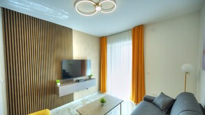 A modern living room with a flat-screen TV mounted on a wooden panel wall, a grey sofa, a yellow armchair, and a marble floor. - Cosy & modern apartment in Paceville CPAC2-1 (St Julian's)