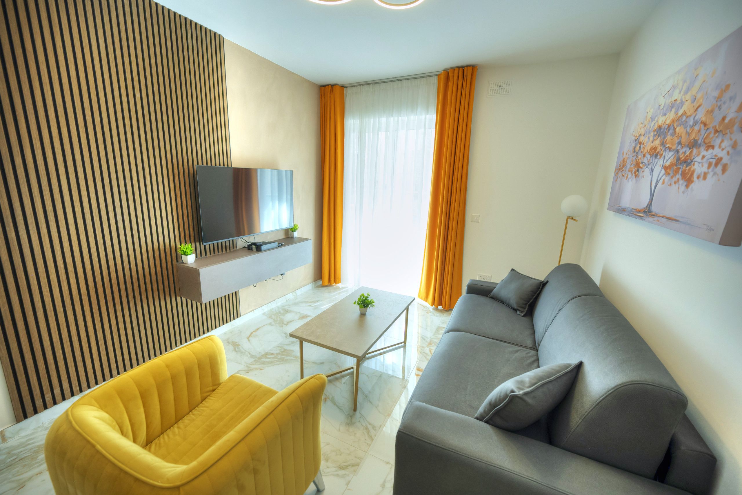 A modern living room with a sofa, a yellow armchair, a TV mounted on the wall, and a painting on the wall.