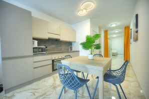 Een moderne keuken met witte kastjes, een marmeren aanrecht en een eethoek met een tafel en stoelen.