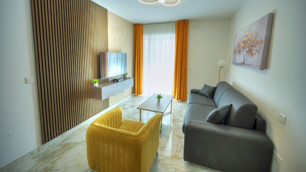 A modern living room with a sofa, a yellow armchair, a TV, and a painting on the wall. - Cosy & modern apartment in Paceville CPAC2-1 (St Julian's)