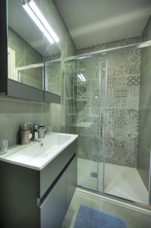 Een moderne badkamer met een douchecabine van glas, een wit wastafelmeubel met een spiegel erboven en wandtegels met een patroon.