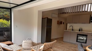 Une cuisine moderne dotée d’un four encastré et d’un réfrigérateur, un coin repas avec deux chaises rembourrées et une petite table, et une grande porte-fenêtre coulissante donnant sur un espace extérieur.