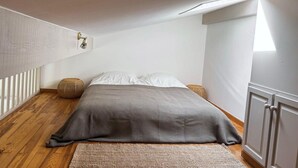 Une chambre à coucher avec un lit, une lampe de chevet, une fenêtre et un plancher en bois.
